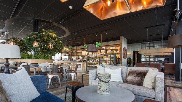 Un espacio lounge moderno con asientos, un bar de café y una planta grande.