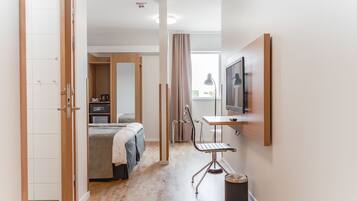 A modern hotel room with a bed, a desk, a chair, a TV, and a window with curtains.