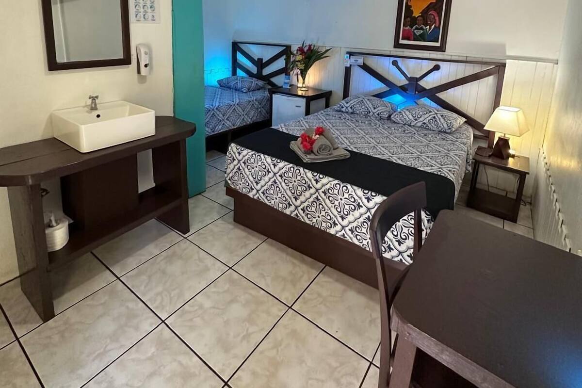 A hotel room with a bed, bedside table, desk, chair, and a bathroom with a sink and mirror.