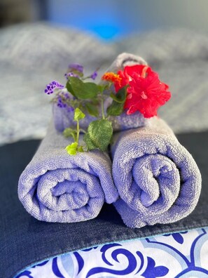 Two rolled towels with purple fabric and a small bouquet of flowers on a dark surface. - Hotel Maritza (Cahuita)