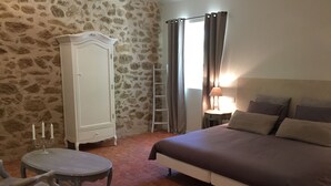 A bedroom with a bed, a wardrobe, a table with candles, a chair, a ladder, and a window with curtains. - La Rivayne (Lauris)