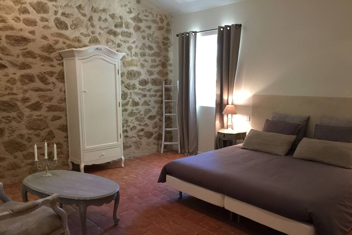 Ein Schlafzimmer mit einem Bett, einem Kleiderschrank, einem Tisch mit Kerzen, einem Stuhl, einer Leiter und einem Fenster mit Vorhängen.