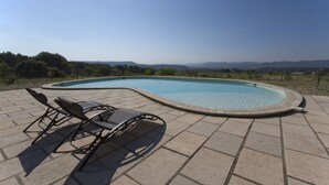 A swimming pool with lounge chairs on a tiled patio, surrounded by a landscape with distant hills. - La Rivayne (Lauris)