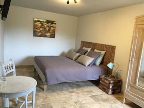 A bedroom with a bed, a chair, a table, and a painting on the wall. - La Rivayne (Lauris)