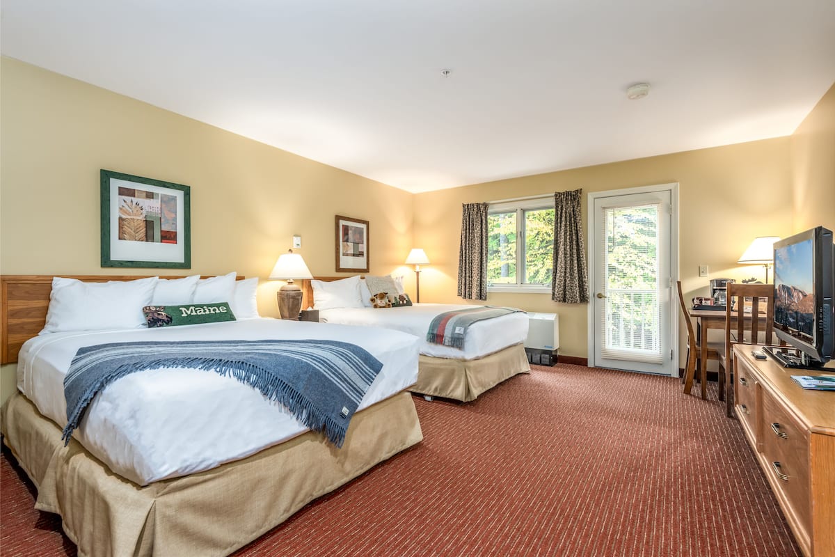 A hotel room with two beds, a television, a desk, and a window with curtains.