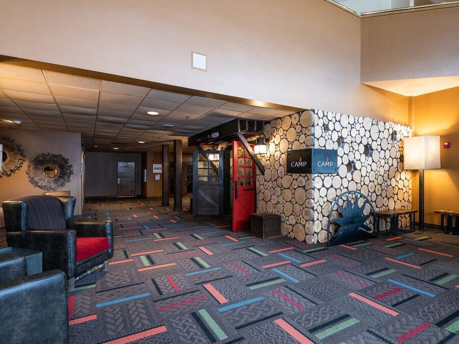 A lobby with a patterned carpet, leather seating, a wall with a log design, and a sign reading "CAMP".