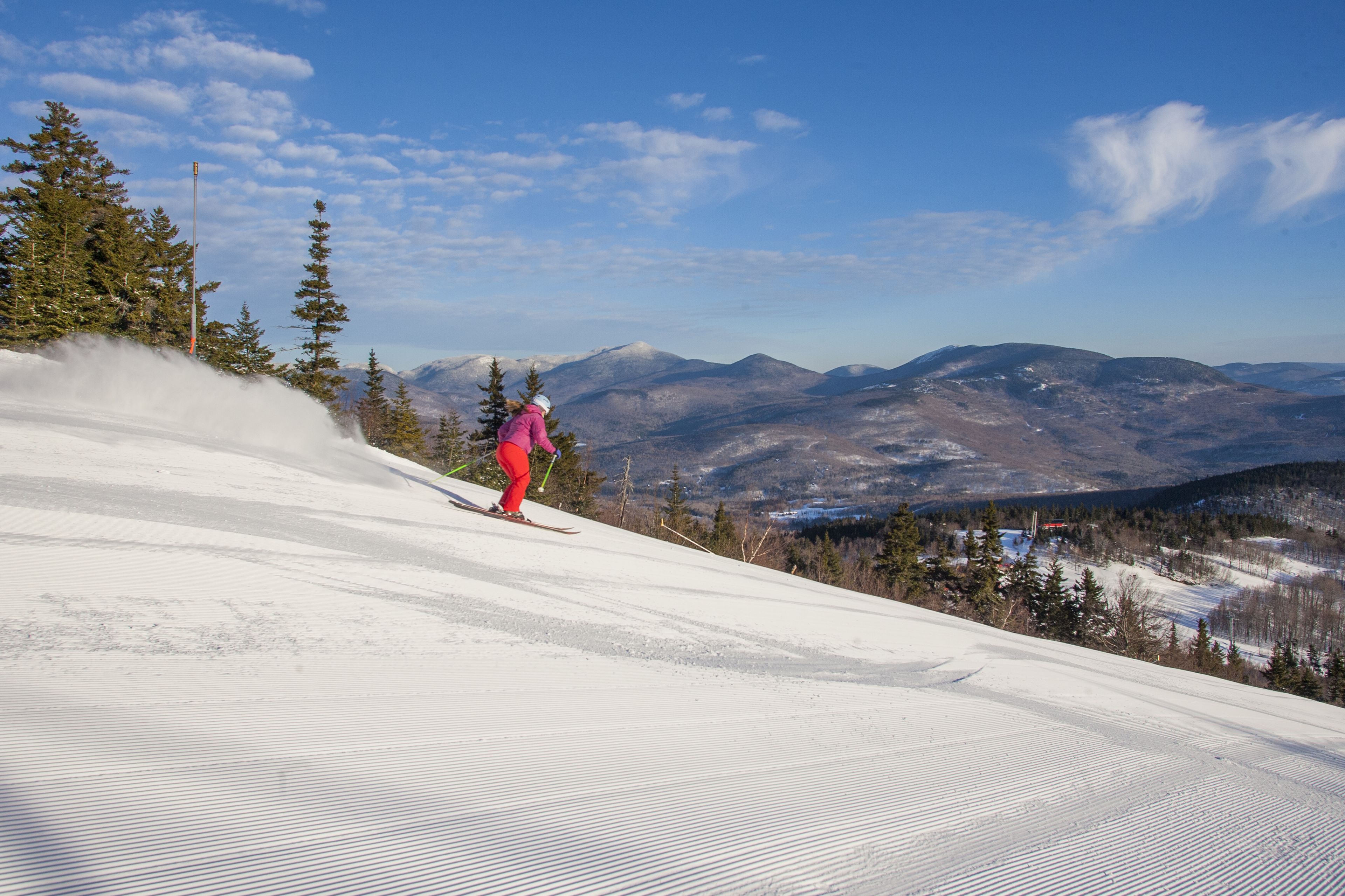 A ski slope with a skier in red pants and a pink jacket.