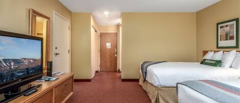 A hotel room with a television on a wooden dresser, a bed with a 'Maine' pillow, and a framed picture on the wall.