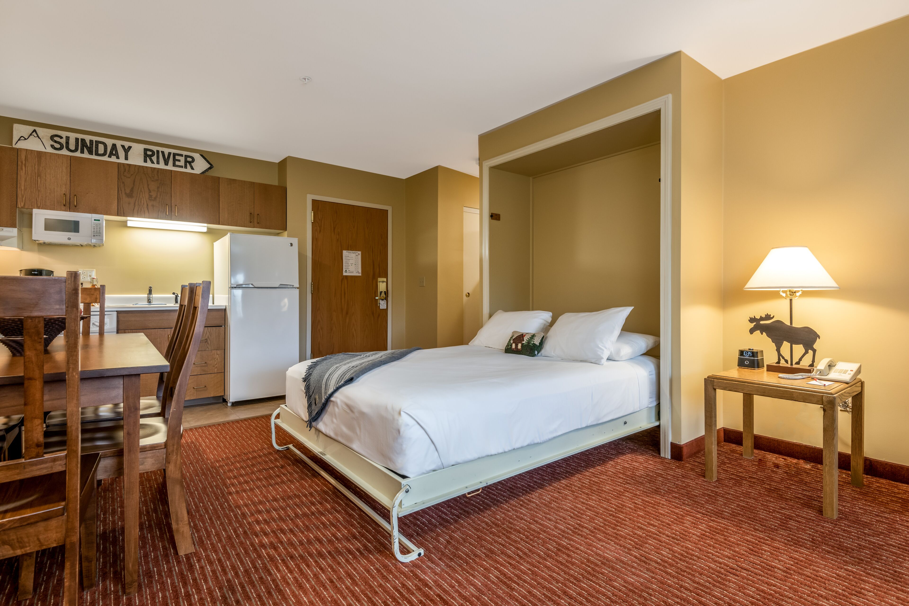 A hotel room with a bed, a desk, a microwave, a refrigerator, and a sign indicating the direction to Sunday River.