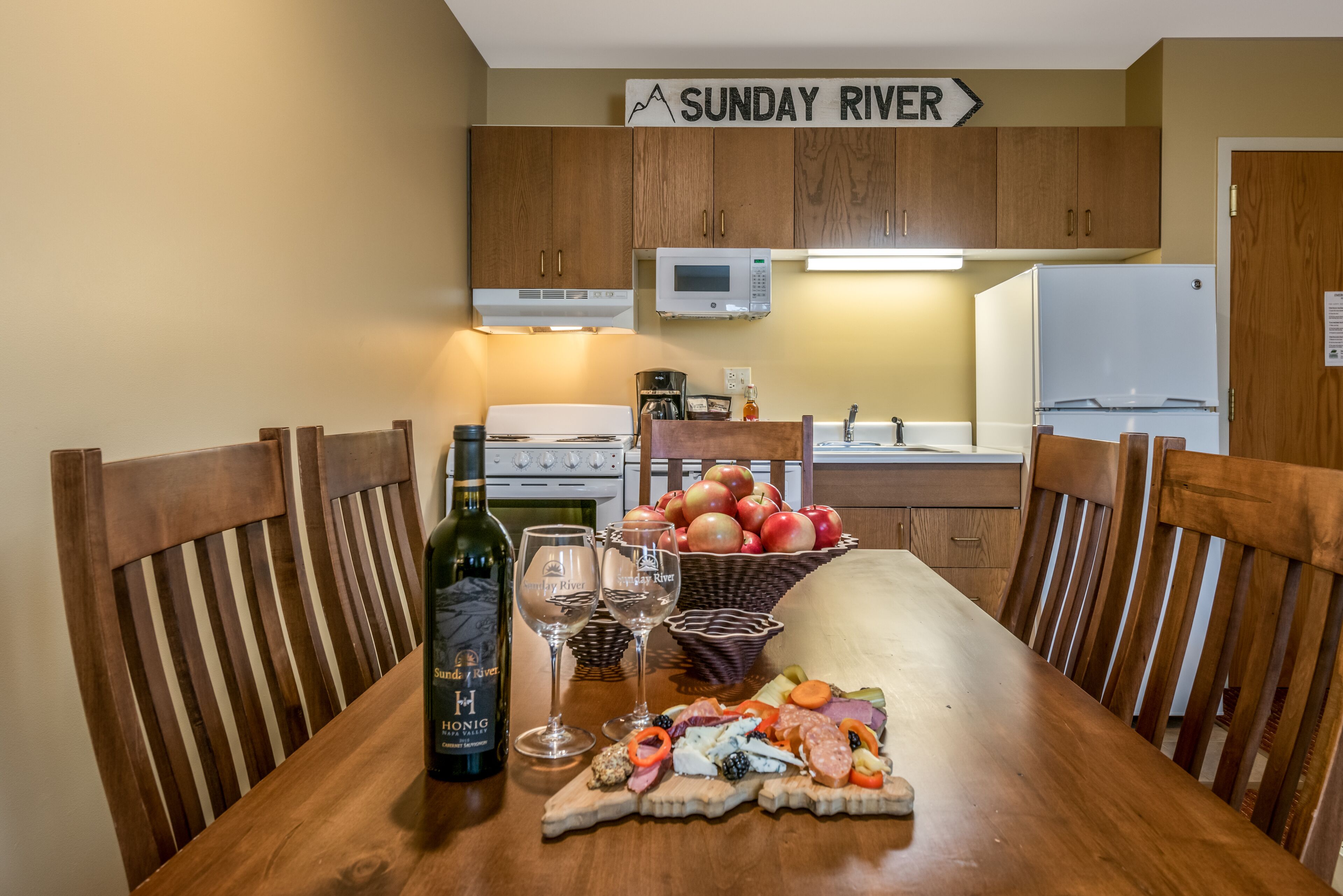 A wooden dining table with a bottle of wine, glasses, and a charcuterie board.