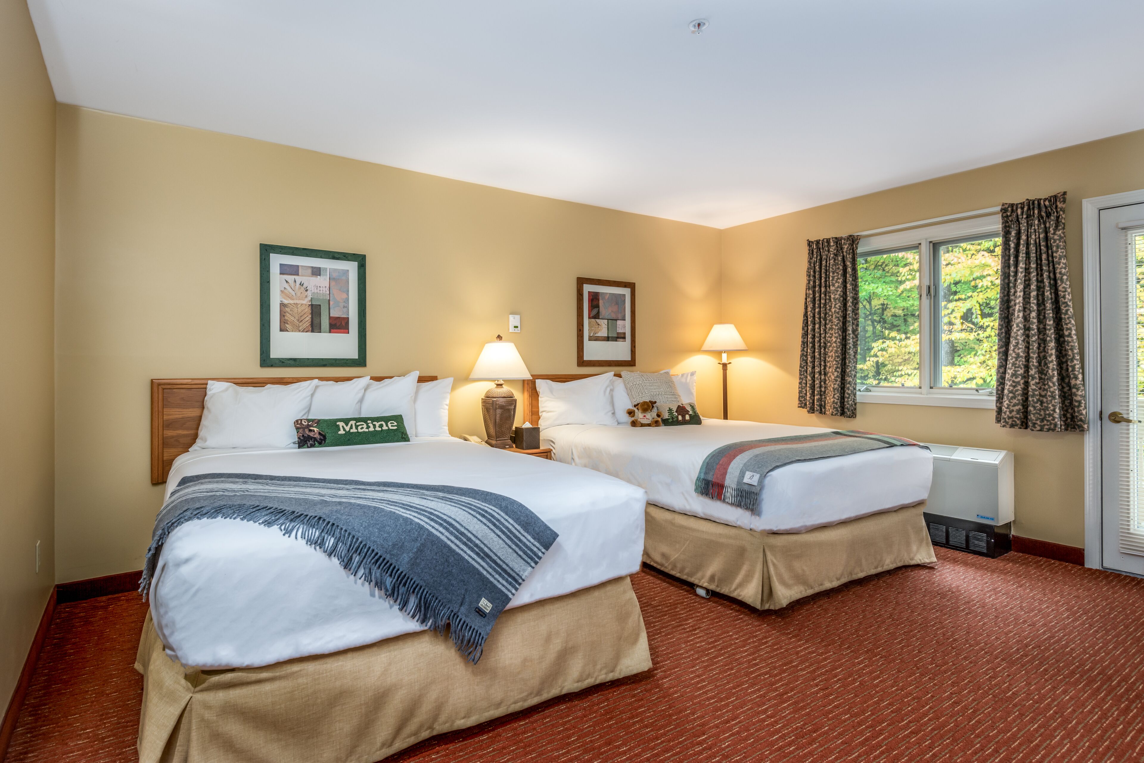 A hotel room with two beds, a window with curtains, and a radiator.
