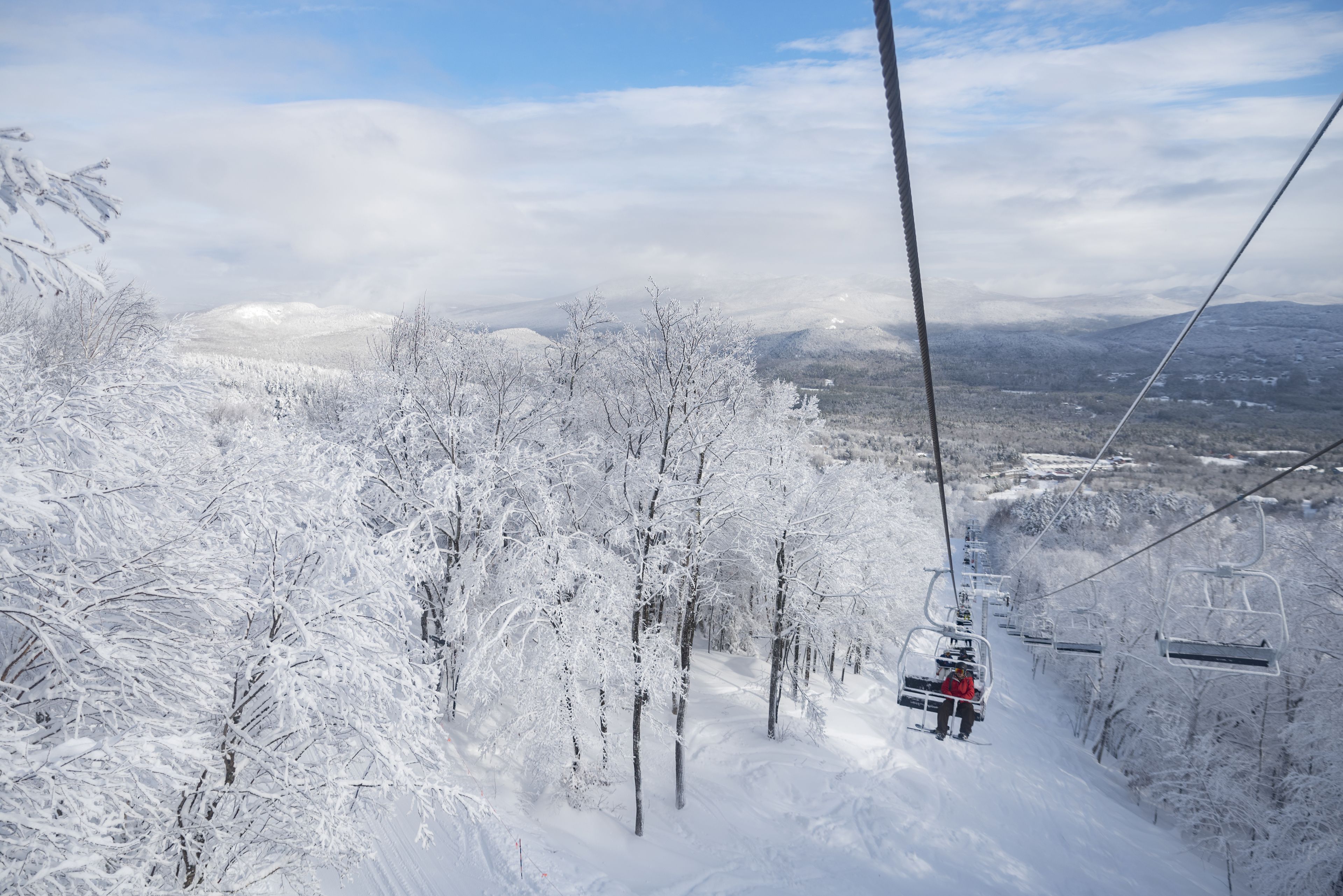 A ski lift with a snowy landscape and trees in the background.