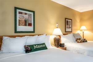 Habitación de hotel con dos camas, cada una con ropa de cama y almohadas blancas. Una cama tiene una almohada con la palabra 