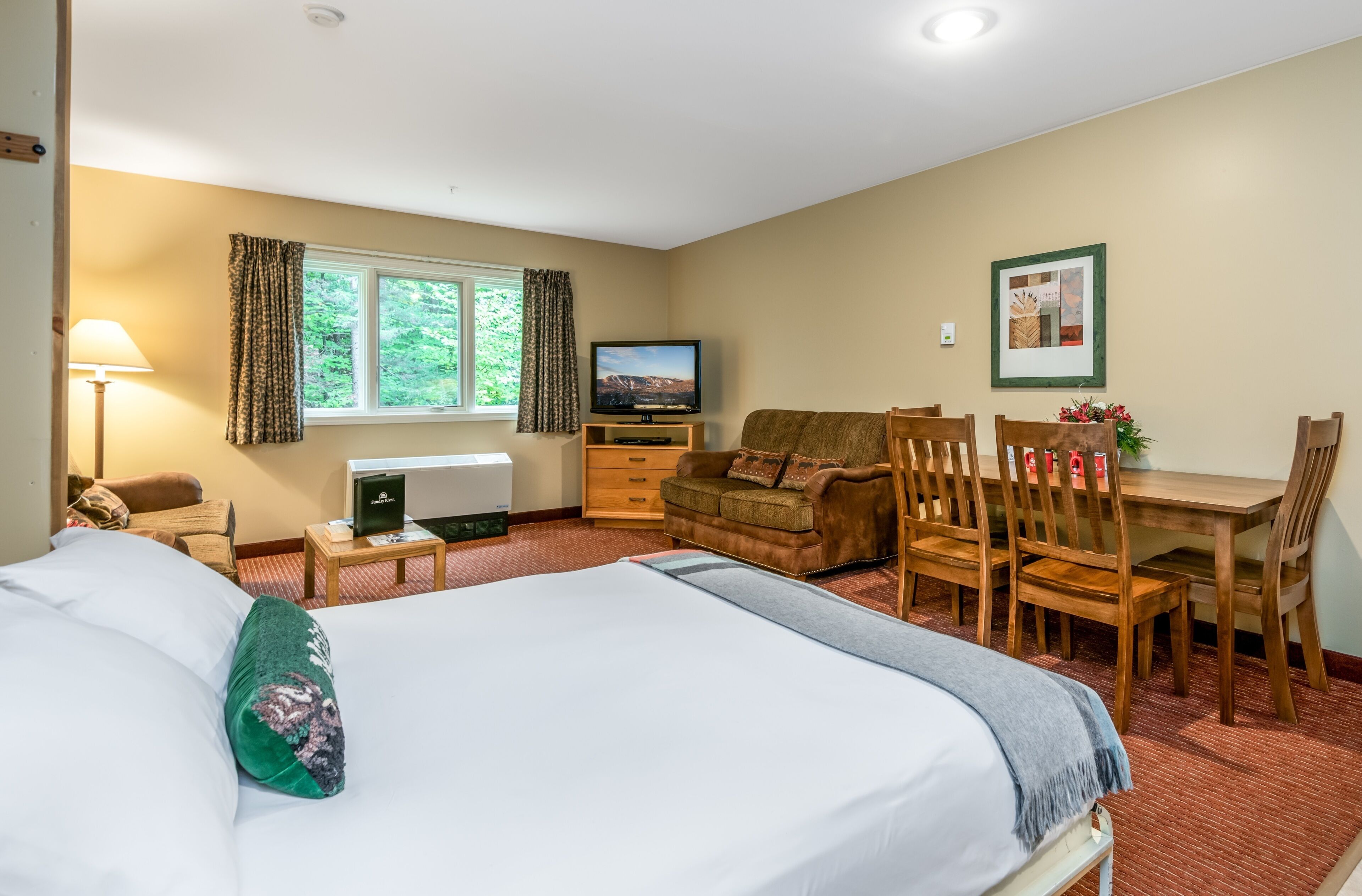 A hotel room with a large bed, a desk with a computer, a television, and a dining area with chairs.