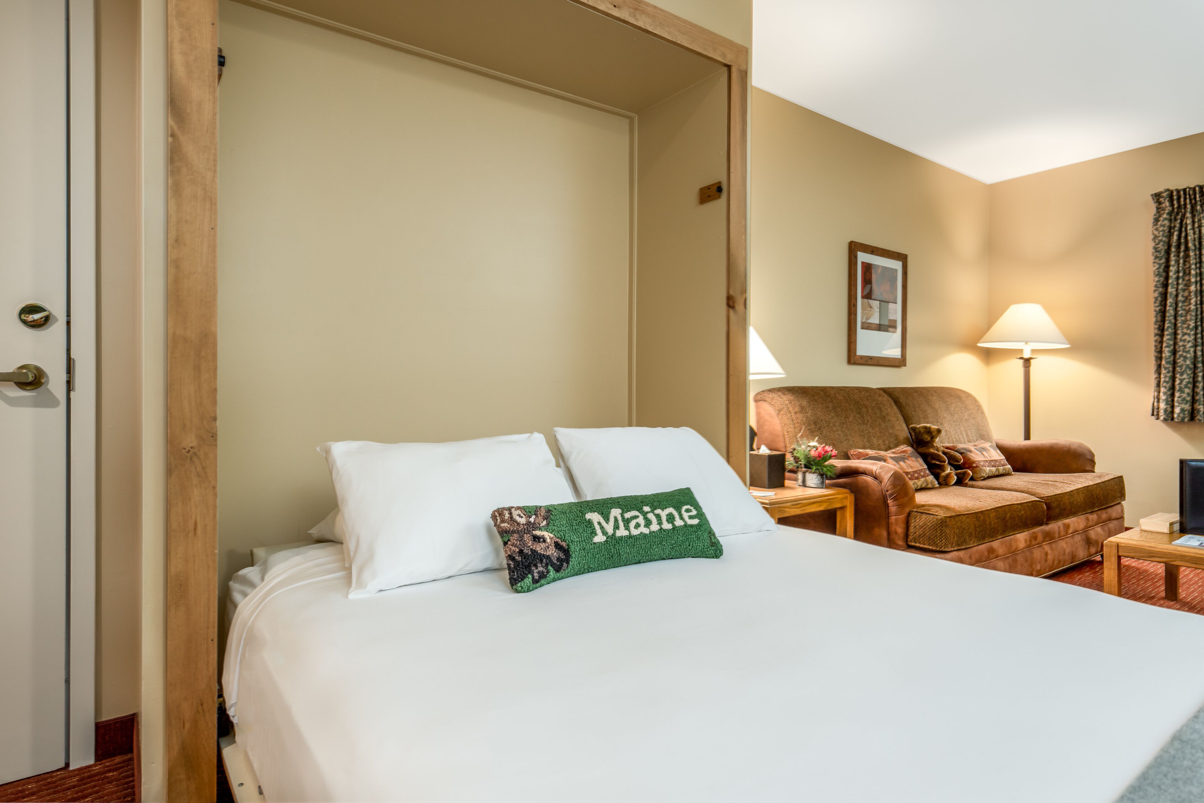 A hotel room with a bed, a chair, a lamp, and a wall-mounted picture.