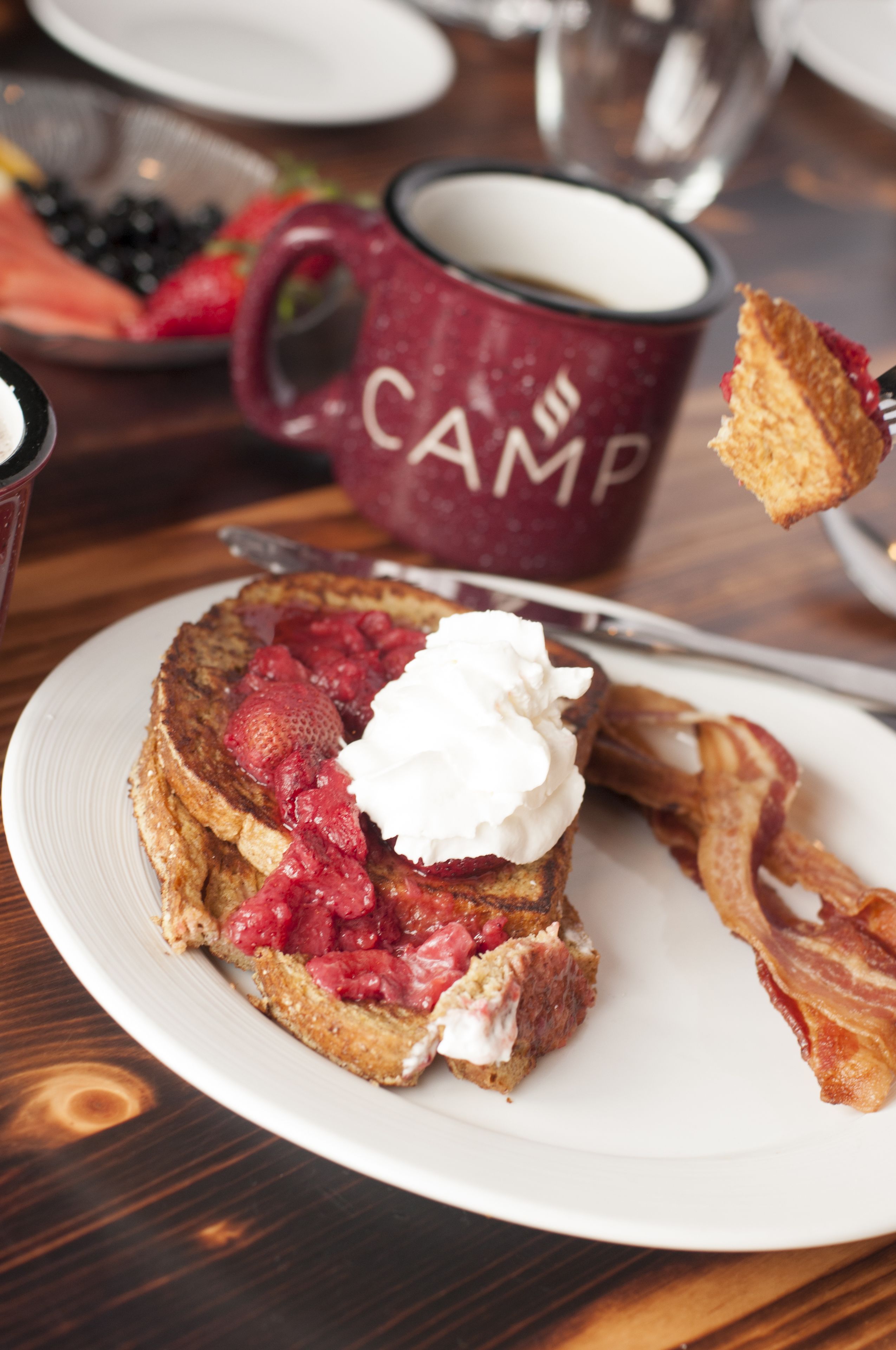 A breakfast plate with toast, strawberries, whipped cream, and bacon.