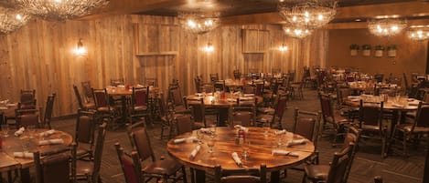 A large dining area with round tables and chairs, wooden walls, and decorative chandeliers.