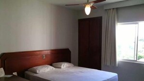 A bedroom with a wooden bed, a nightstand, a ceiling fan, and a window with curtains. - Agape - Hot Springs Apart Hotel (Caldas Novas)