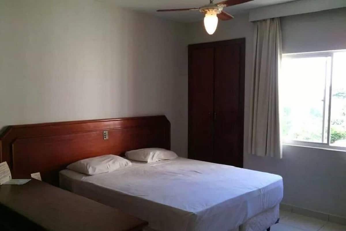A bedroom with a wooden bed, a nightstand, a ceiling fan, and a window with curtains.