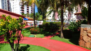 A hotel courtyard with a red pathway, palm trees, and a variety of plants. - Agape - Hot Springs Apart Hotel (Caldas Novas)