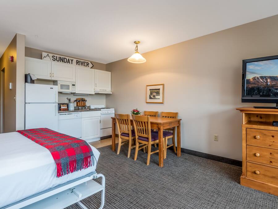 A compact hotel room with a bed, a kitchenette, a dining area, and a TV.
