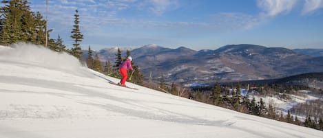 A ski slope with a skier in red pants and a pink jacket.