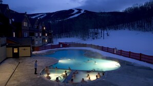 Una piscina al aire libre climatizada rodeada de nieve, con una montaña al fondo.