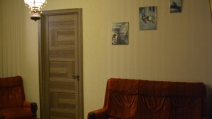 Un salon doté d’un parquet, d’un canapé marron, d’un fauteuil marron, d’une table basse en bois et d’un lustre.
