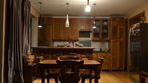 Une cuisine avec des meubles de rangement en bois, une table à manger avec des chaises et des luminaires suspendus.