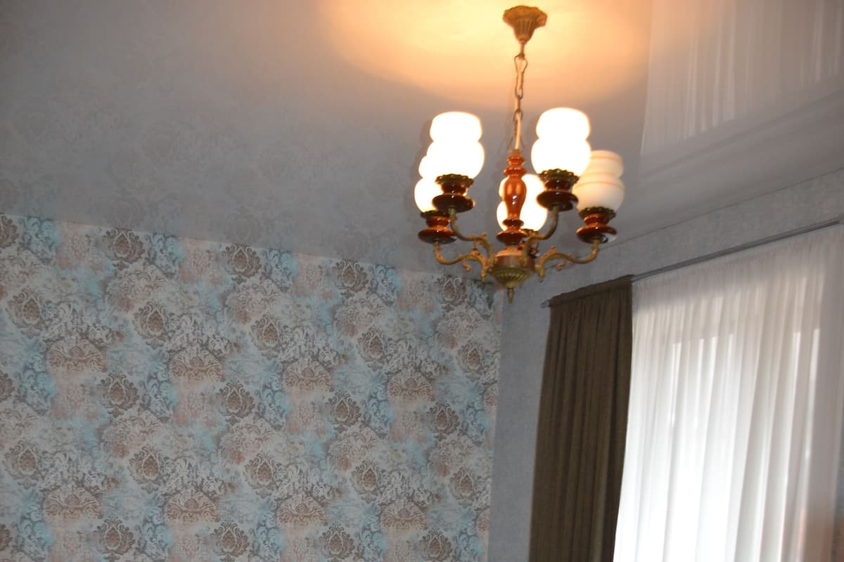 Un dormitorio con cama de madera, una mesita de noche, una silla, papel tapiz estampado y un candelabro.