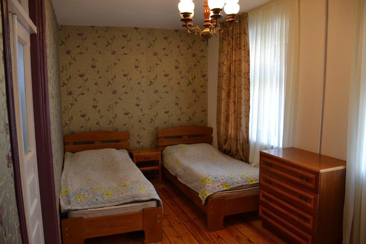 Una habitación con dos camas de madera, un aparador de madera, papel tapiz floral y un candelabro.
