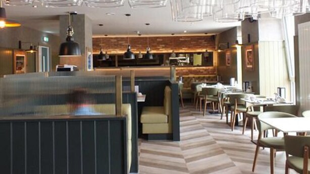 Un restaurante moderno con barra central, mesas en cabinas y suelo con estampado en espiga.