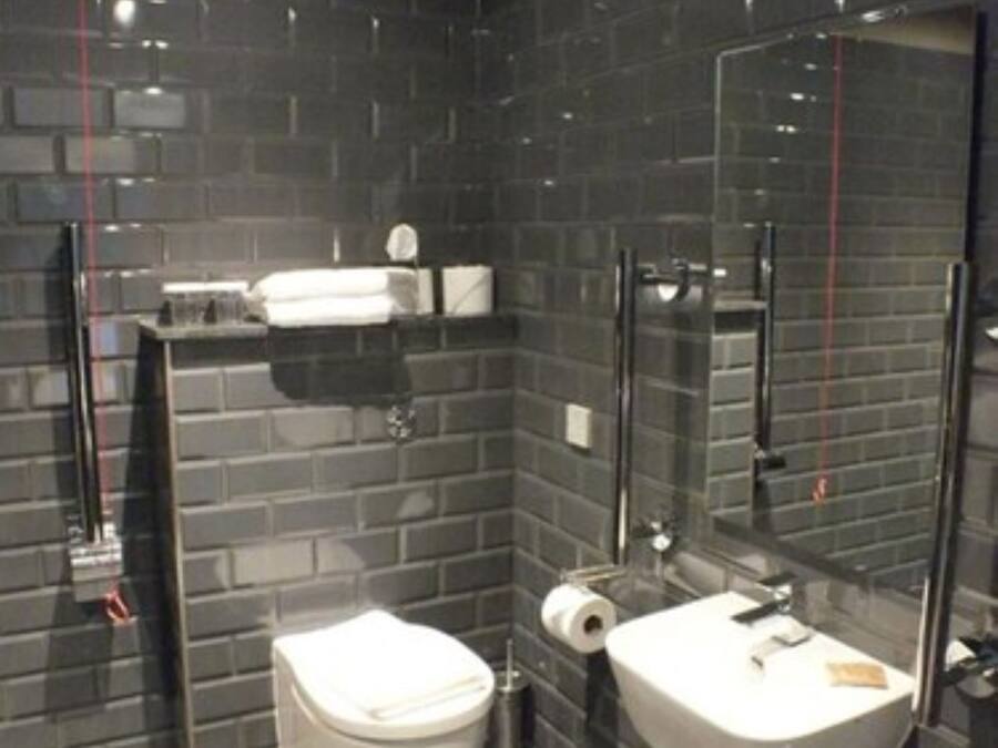 Un bagno moderno con pareti rivestite di piastrelle scure, un water bianco, un lavandino e uno specchio.