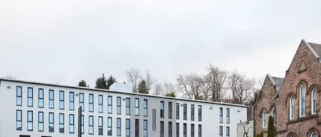Ein modernes Gebäude mit einer Reihe von Fenstern und einem Backsteinbau mit Rundbogenfenstern im Hintergrund.