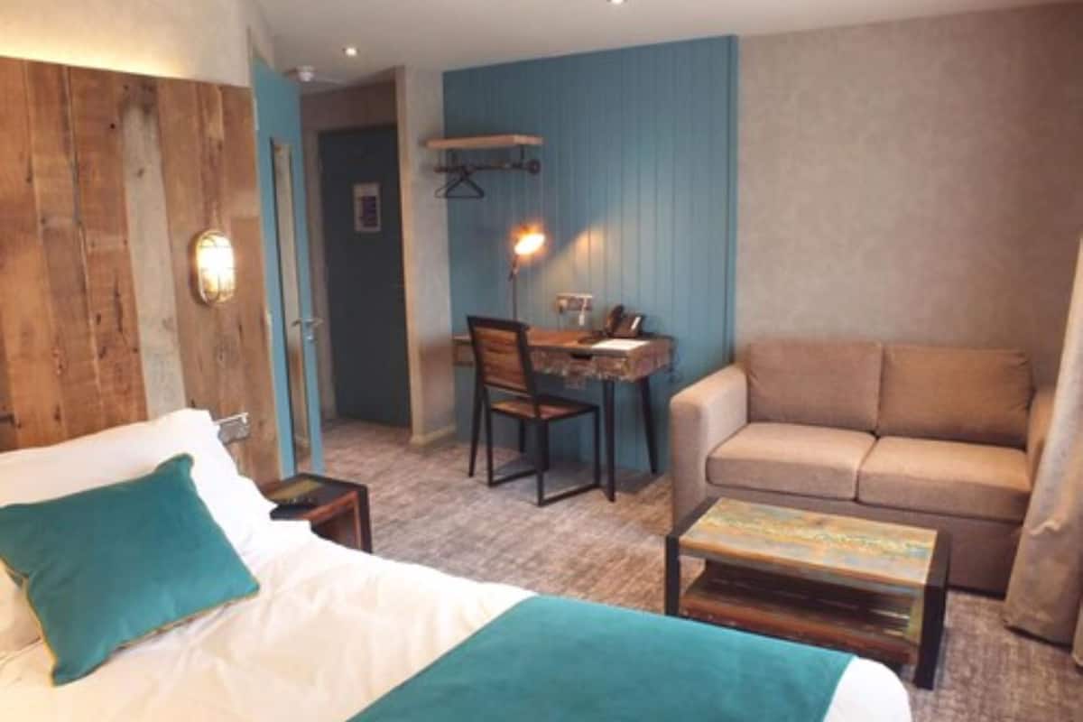 Quarto com cama, sofá, mesa pequena e área de refeições com cadeira e mesa.