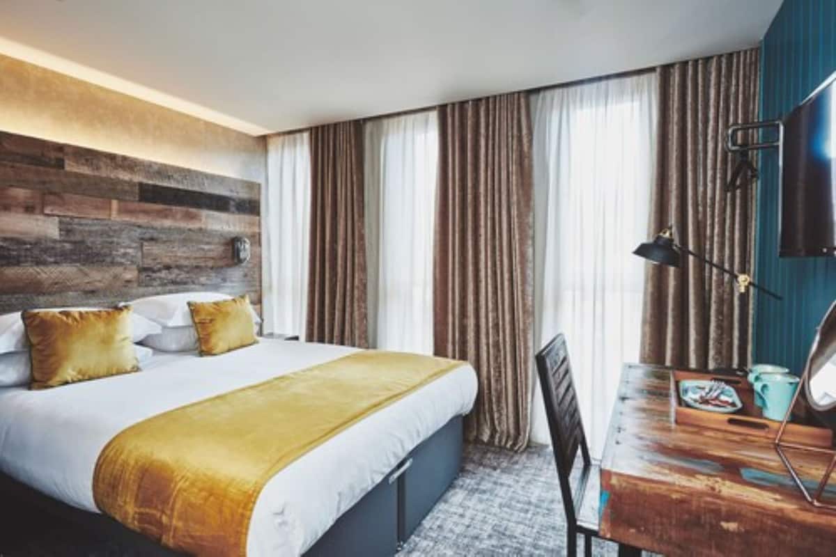 Quarto de hotel com cama, escrivaninha, cadeira e televisão.