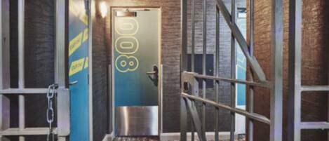 A hallway with a metal staircase, a door with a number, and a wall with yellow tape.