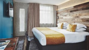 Una habitación de hotel con cama, escritorio, televisor y ventana con cortinas.