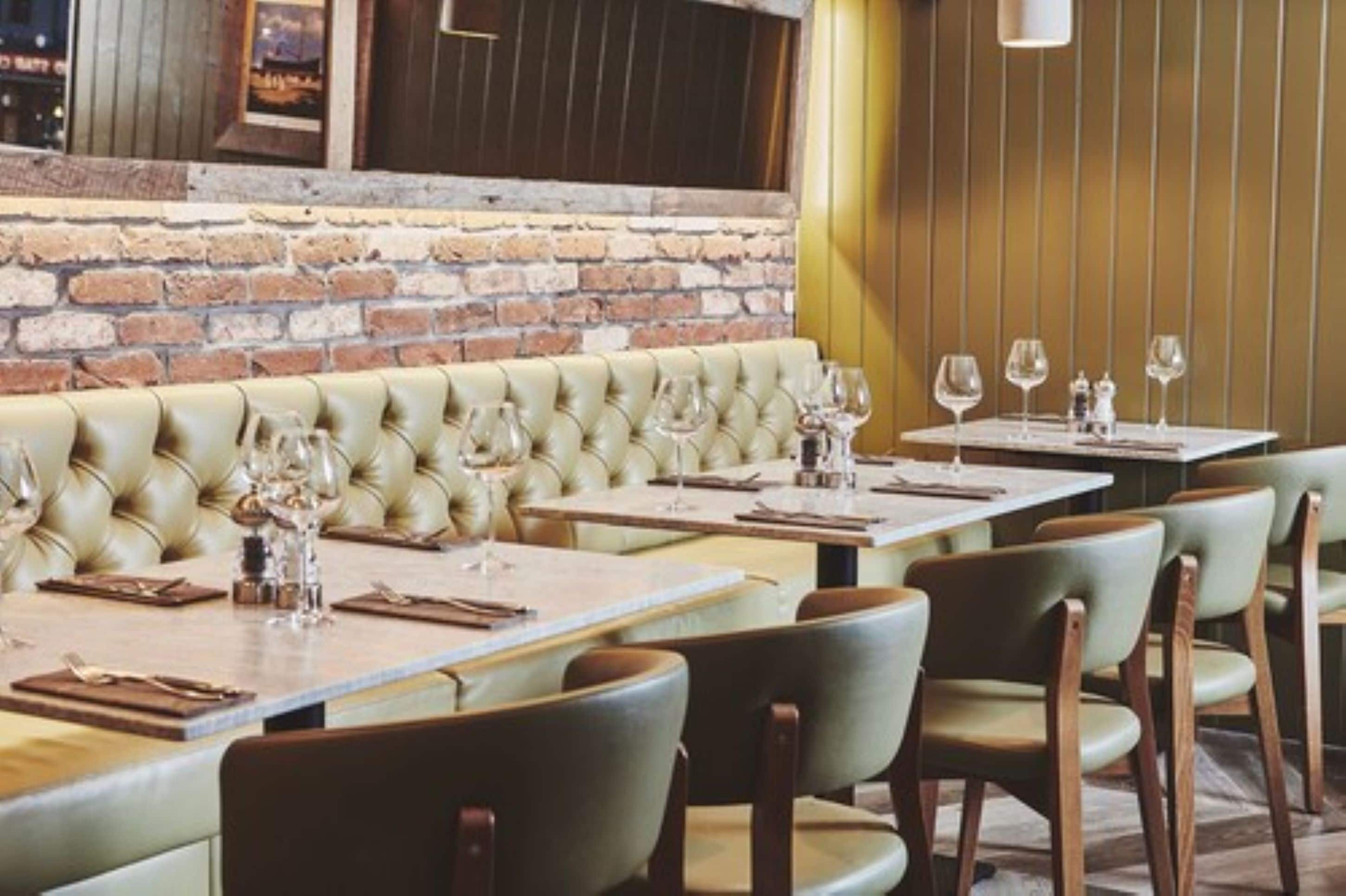 Un restaurante con pared de ladrillo, asientos en cabinas de cuero y mesas de madera con sillas.