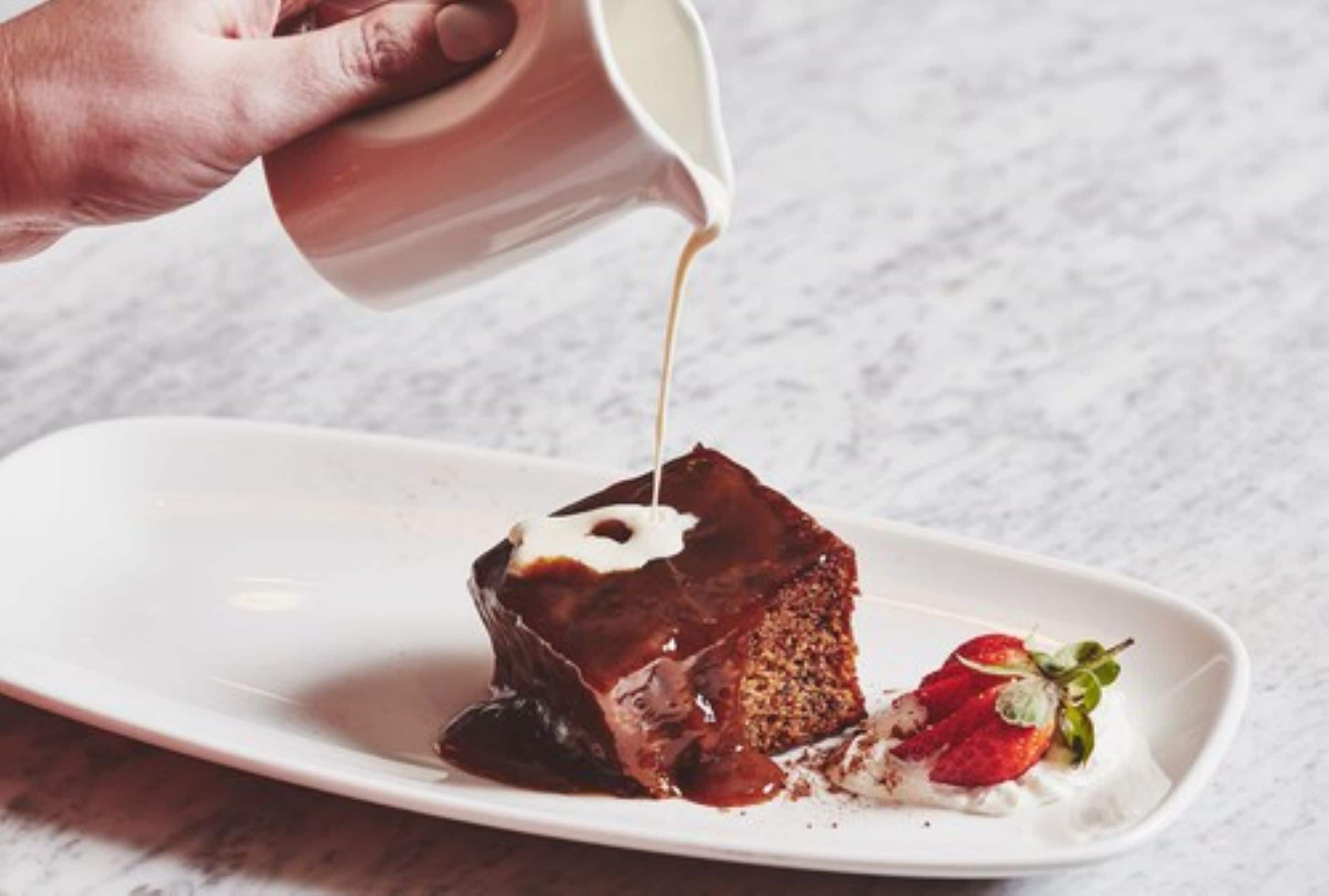 A hand pouring a liquid onto a dessert on a plate.