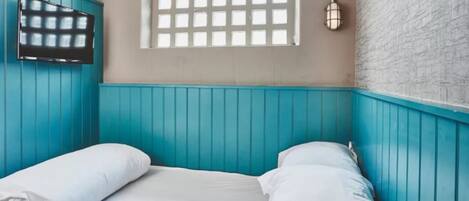 A room with teal walls, a window with a grid pattern, a flat-screen TV mounted on the wall, and two bedside lamps.