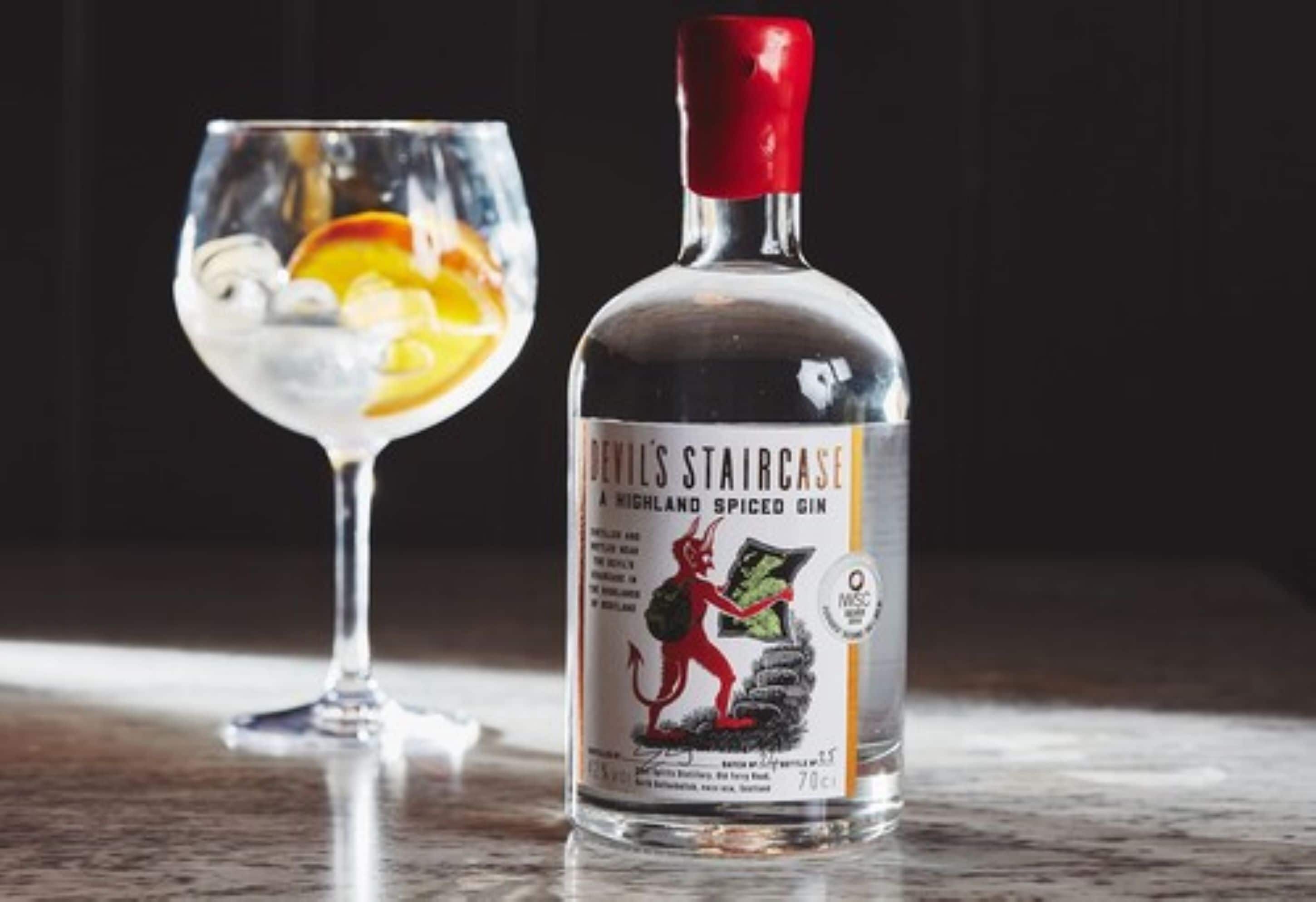 Une bouteille de gin aromatisé aux épices « Devils Staircase Highland » et un verre rempli de glaçons et de tranches de fruits.
