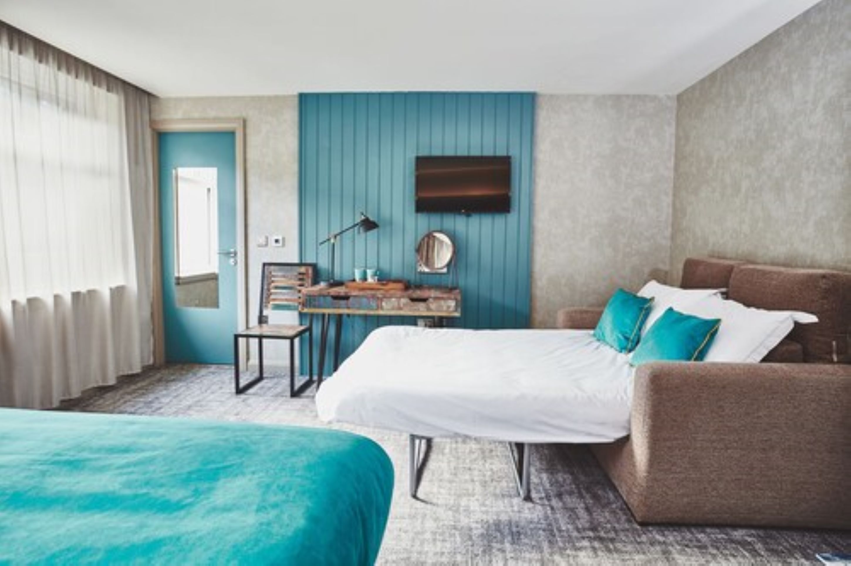 A hotel room with two beds, a desk, a chair, a TV, and a door.