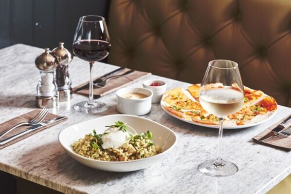 A dining table with a bowl of salad, a plate of pizza, and a glass of white wine.