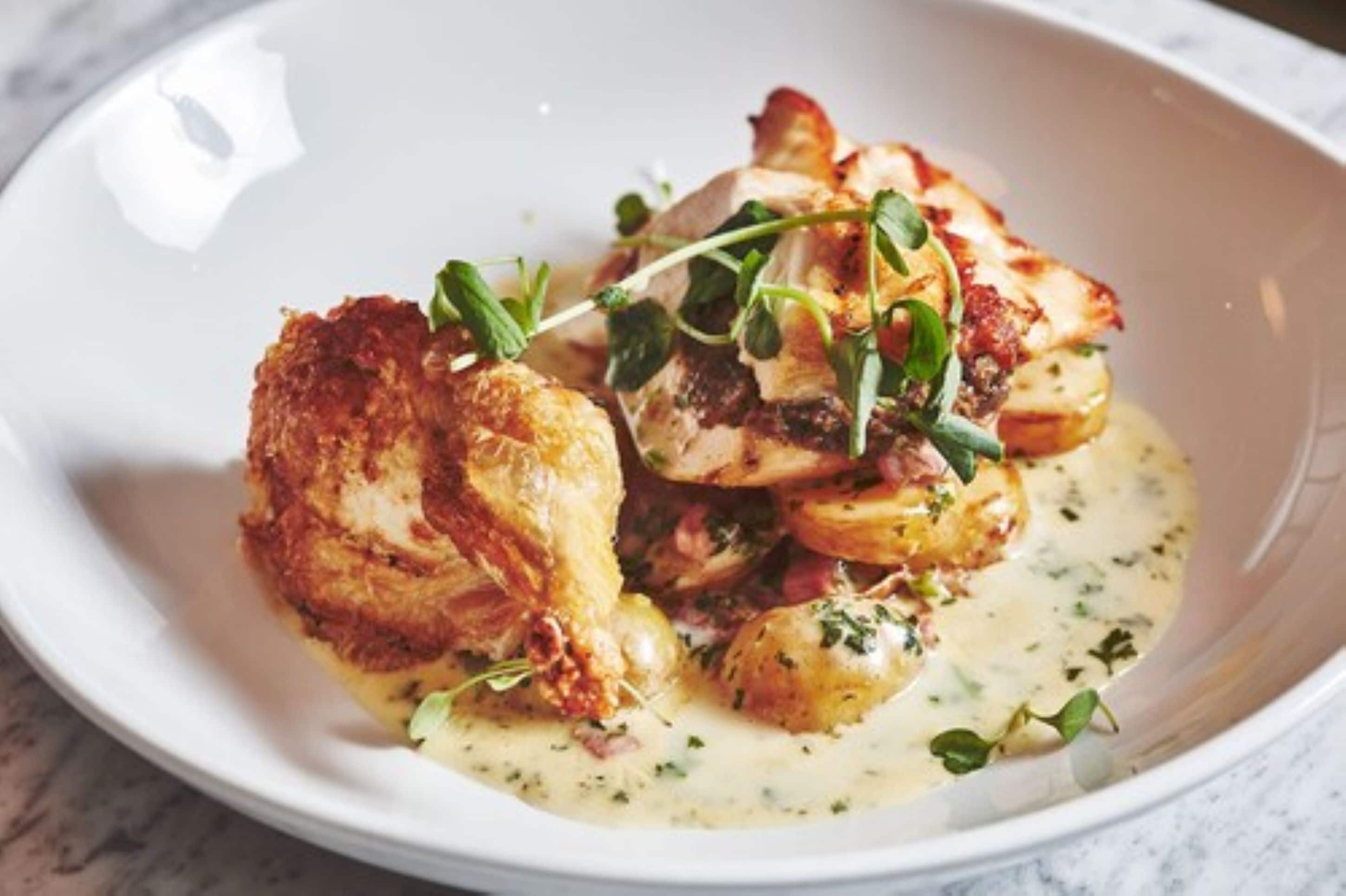 Une assiette blanche contenant un plat de poulet, de pommes de terre et de légumes verts, agrémenté d’herbes.