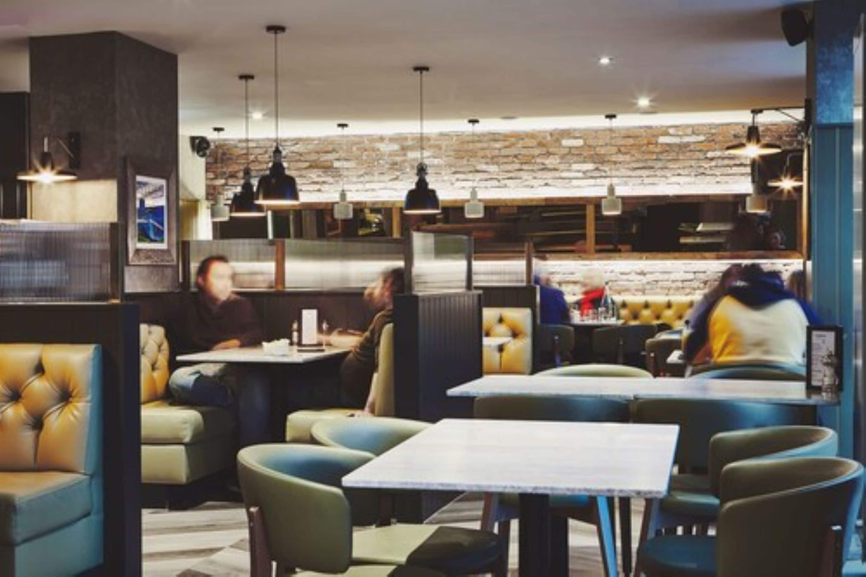 Een modern restaurant met zitjes en tafels, een achtergrond van bakstenen en hanglampen.