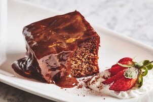 Un postre con salsa de chocolate, una porción de pastel y fresas en un plato.