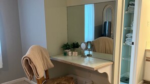A bathroom with a wooden chair, a vanity with a mirror, a small plant, and a laundry basket. - Knee Deep in the Water Somewhere... (Key Colony Beach)