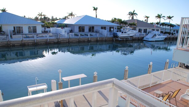 A marina with boats docked, a pool area with lounge chairs, and a building with a blue roof. - Knee Deep in the Water Somewhere... (Key Colony Beach)