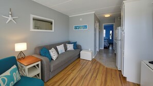 Ein modernes Wohnzimmer mit einem grauen Sofa, einem Holztisch und einem blauen Sessel. Eine weiße Meerstern-Dekoration hängt an der Wand, und ein gerahmtes Bild befindet sich über dem Sofa.